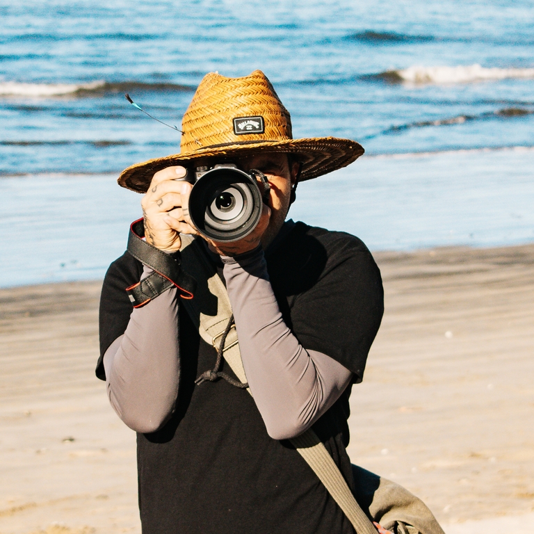 Andy Marin, Nosara surf photographer, shooting from the beach in a straw hat