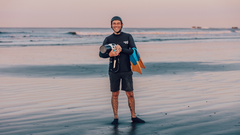 Andy Marin on the beach at dusk with a water-housing camera and swim fins